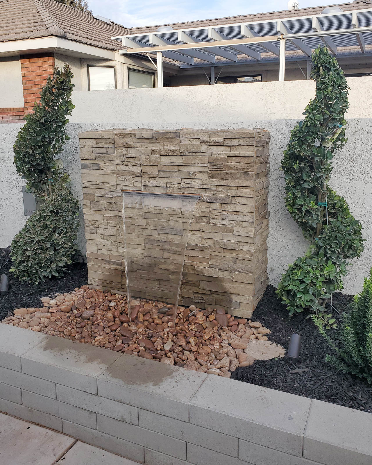 Stacked stone fountain wall with spiral topiaries