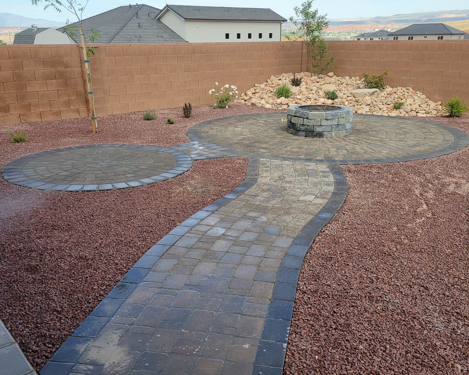 Circular paver patios connected by a curved paver path with fire pit